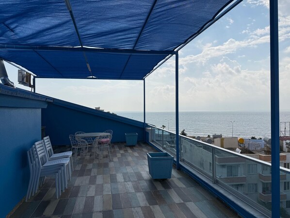 A balcony with a view of the sea, a table with chairs, and a trash bin.