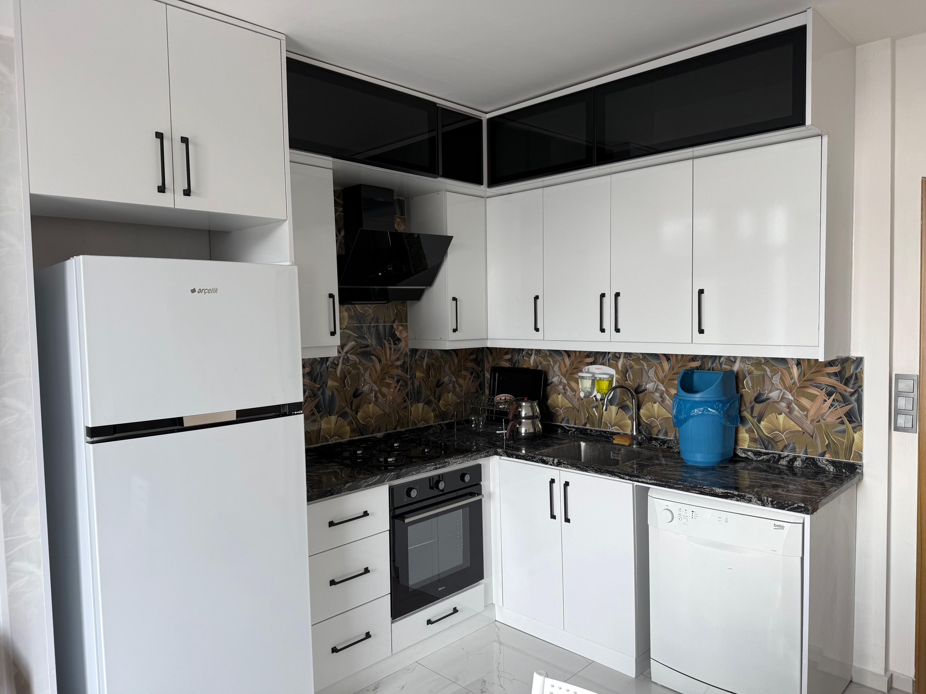 A kitchen with white cabinets, a black oven, a dishwasher, and a marble countertop.
