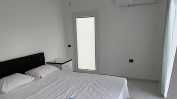 Habitació d'hotel amb un llit, una taula de nit, un aparell d'aire condicionat i una finestra amb persianes.