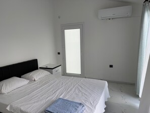 A hotel room with a bed, a nightstand, an air conditioning unit, and a window with blinds.