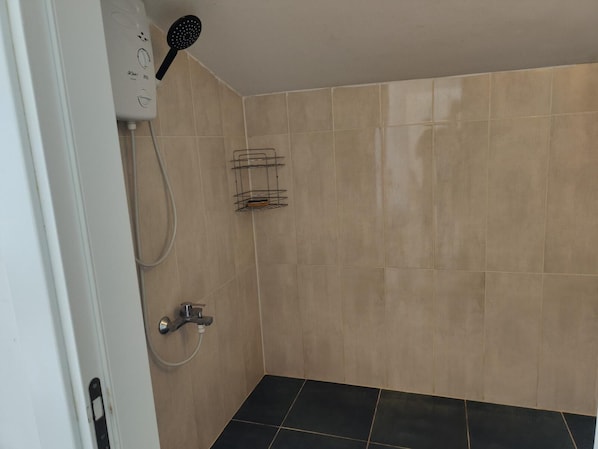 A shower area with beige tiles, a black shower head, and a metal rack.
