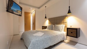 Un dormitori modern amb un llit gran, taules de nit, un televisor penjat i una tauleta de nit amb una làmpada.
