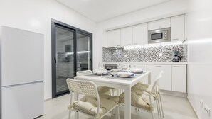 Una cuina moderna amb armaris blancs, microones i un respatller de rajola.