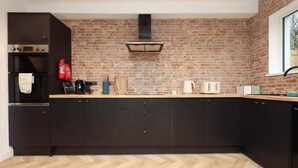 Une cuisine moderne avec des meubles de couleur sombre, un mur en briques et un motif de parquet en chevrons.