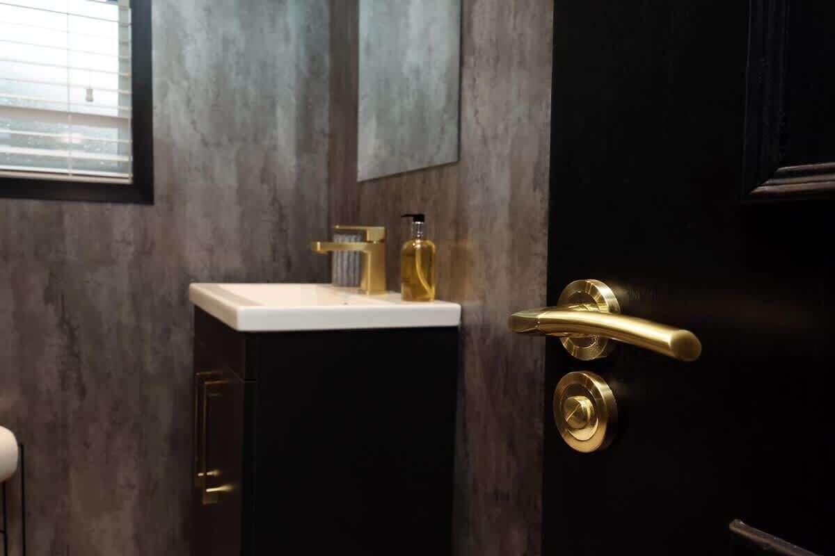 Een badkamer met een witte wastafel, gouden details en een donkere deur.