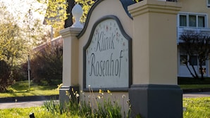 Placa com o nome 'Klinik Rosenhof' em um jardim com grama e flores.