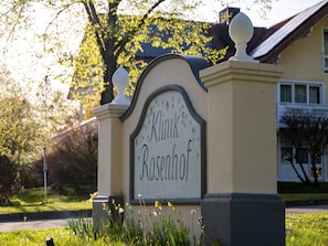 A sign with the name 'Klinik Rosenhof' in a garden setting with grass and flowers. - Gemutliches Studio in Bad Birnbach mit Balkon (Bad Birnbach)