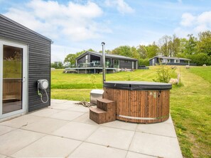 A modern outdoor patio area with a hot tub, wooden steps, and a glass door leading to a covered deck. - 5 Star Holiday Home in Aabenraa (Aabenraa)