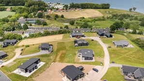 Vista aerea di una zona residenziale con case moderne, un ampio campo aperto e un lago sullo sfondo.