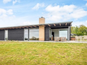 A modern house with a large glass door, a brick chimney, and a patio with outdoor furniture. - 5 Star Holiday Home in Aabenraa (Aabenraa)