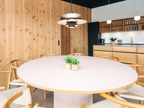 A round table with chairs, a potted plant, and pendant lighting in a room with wooden paneling and a kitchen area. - 5 Star Holiday Home in Aabenraa (Aabenraa)