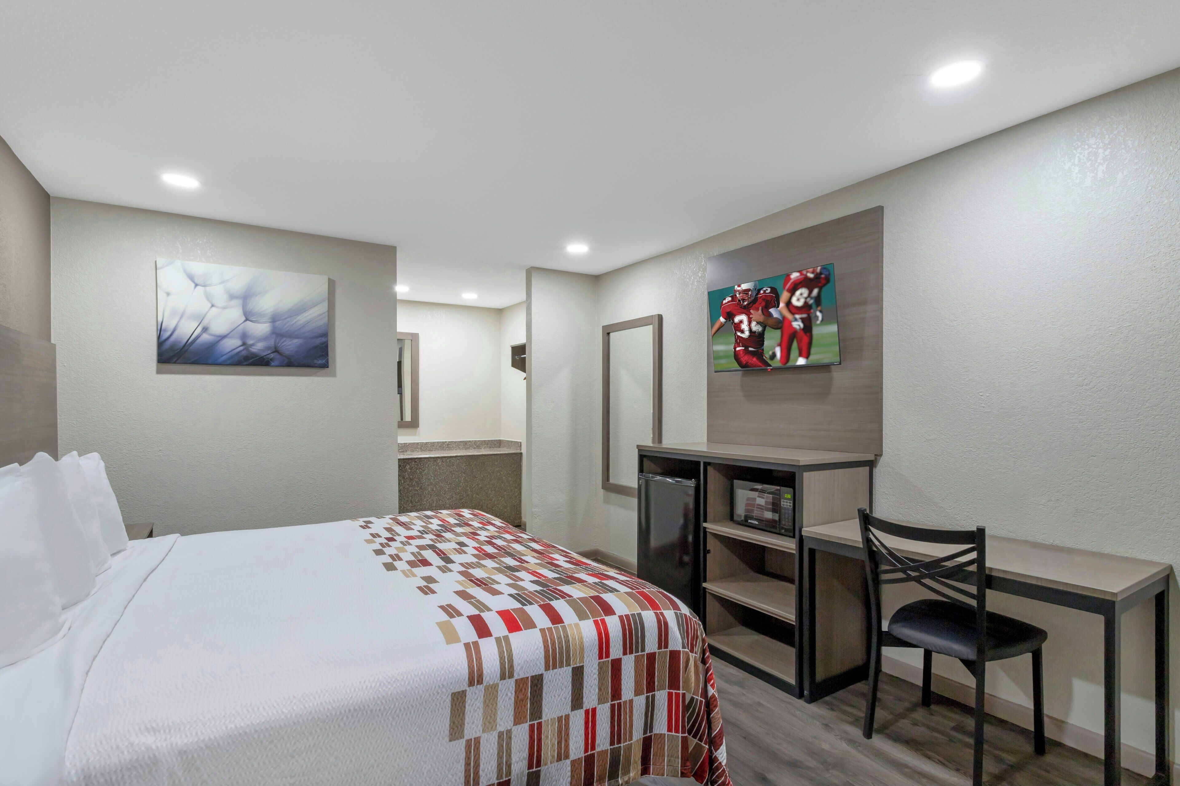 A hotel room with a bed, a desk, a chair, a television, and artwork on the walls.