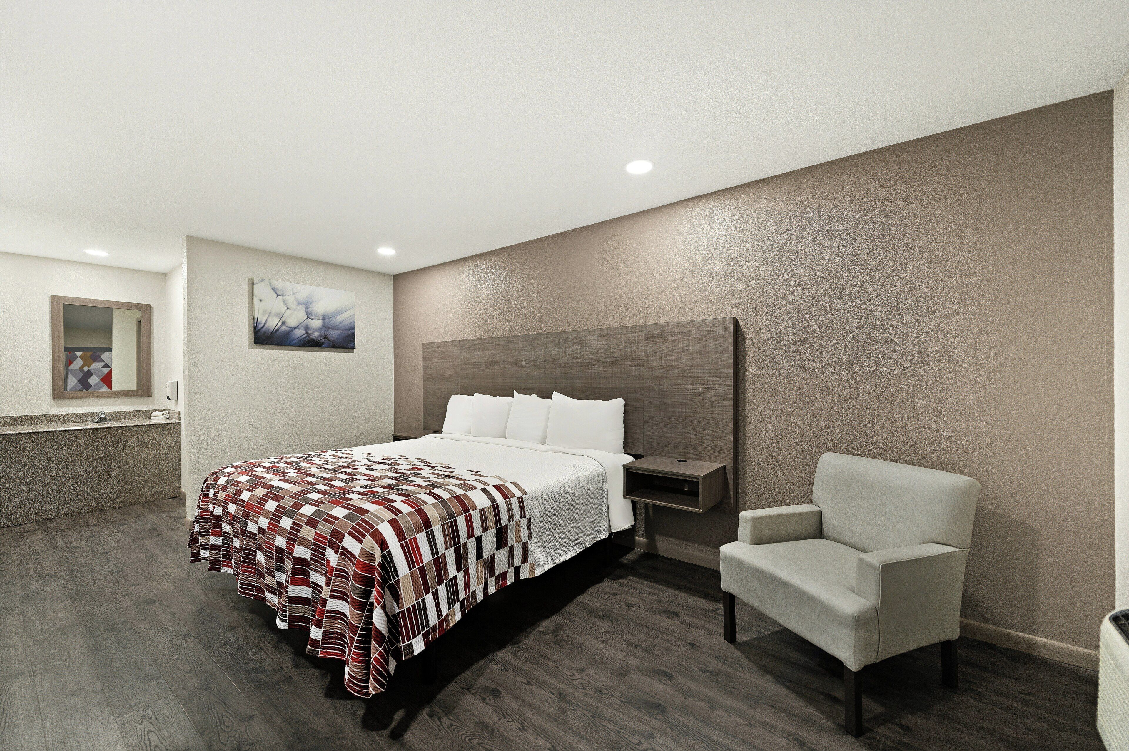 A hotel room with a bed, a chair, a nightstand, and a wall-mounted artwork.