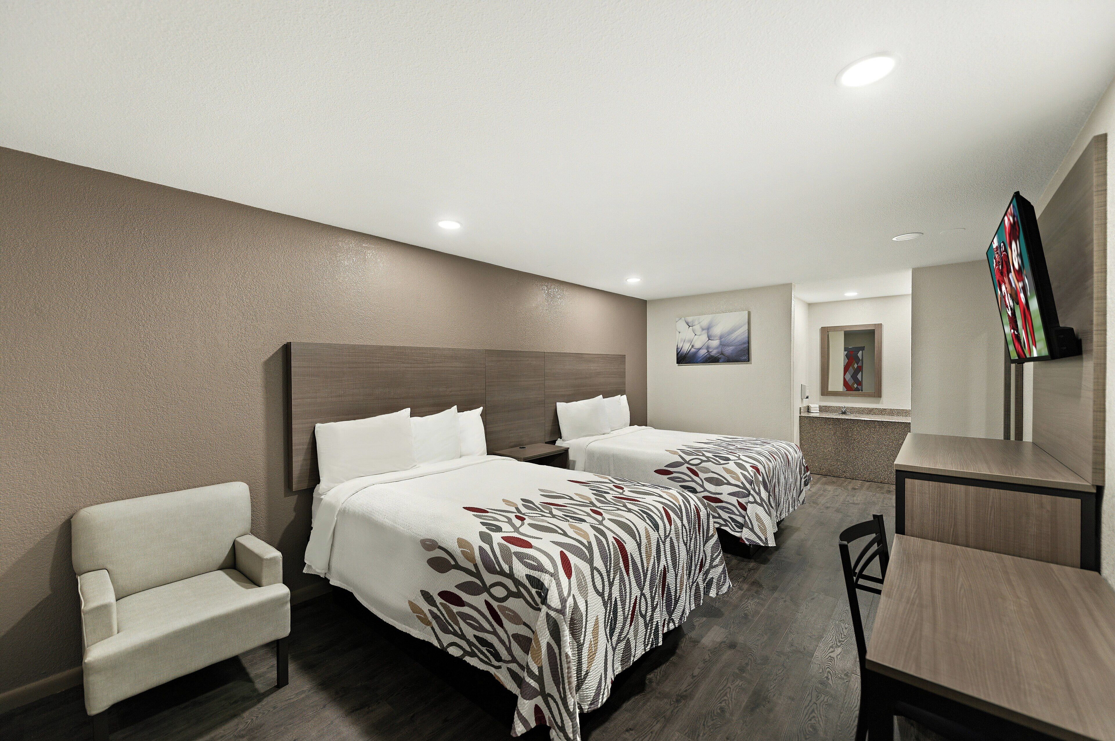 A hotel room with two beds, a desk, a chair, a television, and a bathroom.