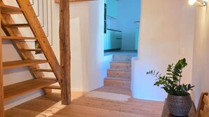 A wooden staircase leading to a second floor, a potted plant on a table, and a view of a kitchen area. - Cavigliano Rustic (Cavigliano)