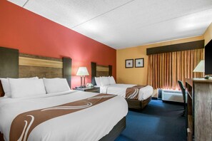 Ett hotellrum med två sängar, ett skrivbord, en lampa och ett fönster med gardiner.