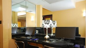 Habitación de hotel con dos escritorios, cada uno con una computadora y una silla. Un espejo en la pared, una lámpara y una puerta con espejo.