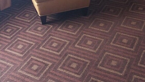 Una habitación de hotel con un sillón rojo, una pequeña mesa redonda y una alfombra estampada.