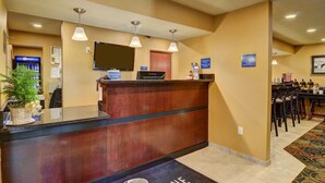 A hotel reception area with a wooden reception desk, a flat-screen TV, and a vending machine. - Cobblestone Hotel Suites Punxsutawney Pa (Punxsutawney)