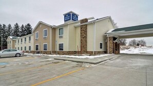 A hotel with a two-story structure, a covered parking area, and a snow-covered ground. - Cobblestone Hotel Suites Punxsutawney Pa (Punxsutawney)