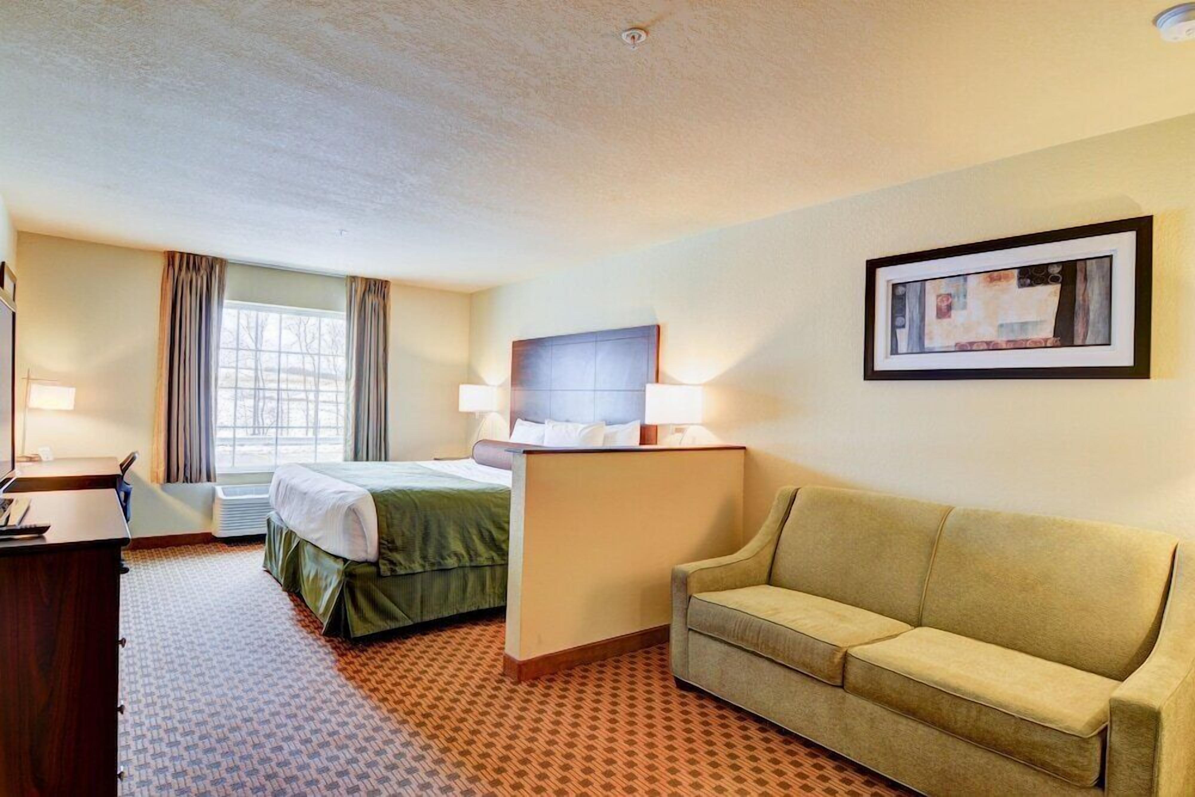 A hotel room with a bed, a desk, a couch, and a framed picture on the wall.