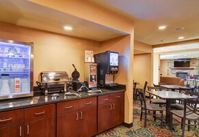 Quarto de hotel com cozinha compacta, máquina de café, micro-ondas e geladeira. Há também mesas e cadeiras na área de jantar.
