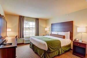 Quarto de hotel com uma cama grande, uma escrivaninha, uma cadeira, um telefone e uma janela com cortinas.