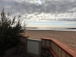 A beach with a stone wall and a metal gate. - Ground-floor apartment in a villa overlooking the beach (Valras-Plage)