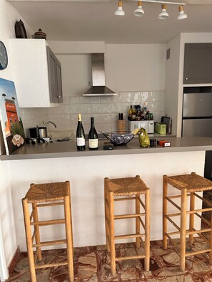 A kitchen with a central island, bar stools, a microwave, and a refrigerator. - Ground-floor apartment in a villa overlooking the beach (Valras-Plage)