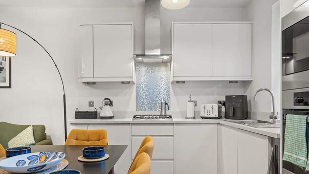 A modern kitchen with white cabinets, a black countertop, and a dining area with a table and chairs. - Brand-new Fulham Stay Near Thames (London)