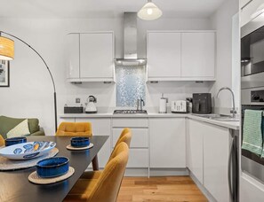 Een moderne keuken met witte kasten, een zwart aanrecht en een eethoek met een tafel en stoelen.