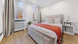 Un dormitorio moderno con una cama grande, una mesita de noche, un radiador y una ventana con vistas a edificios.