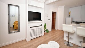 Una sala de estar moderna con televisor, muebles blancos, un espejo y una planta.