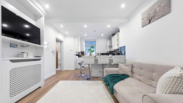 Una sala de estar moderna con un sofá, un televisor y una cocina al fondo.