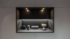 Un'elegante unità espositiva dal design minimalista e moderno, nera, con una fotocamera, una piccola scatola nera e una ciotola bianca decorativa.