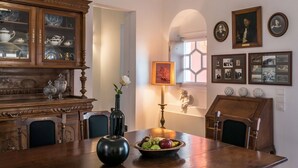 Una sala da pranzo con un tavolo in legno, una ciotola di frutta, un vaso con fiori, un mobiletto con vetrate e quadri appesi al muro.