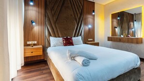 Une chambre d’hôtel moderne avec un grand lit, une tête de lit en bois, des tables de chevet et un miroir.