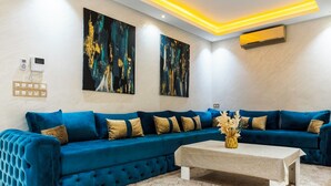 Un salon moderne avec un canapé d’angle bleu, un sol à motifs de marbre et des œuvres d’art abstraites accrochées aux murs.