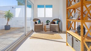 Una habitación iluminada por el sol con dos sillones de mimbre, una mesita y un estante de madera.