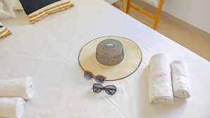 Una cama bien hecha con sábana blanca, un sombrero de paja, gafas de sol y toallas enrolladas.
