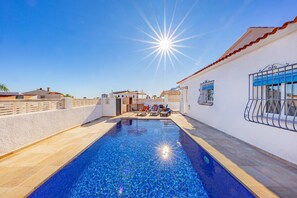 A swimming pool with a clear blue water, surrounded by a white building with a tiled roof and a metal gate. - Villa Kuki - PlusHolidays (Calpe)