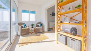 Un salón luminoso con muebles de mimbre, una estantería de madera y un ventanal grande.