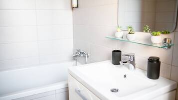 Ein modernes Badezimmer mit einem weißen Waschbecken, zwei Wasserhähnen, einem Spiegel und einer Glasablage mit Blumentöpfen.