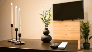 A wooden table with three white candles, a vase with green foliage, a remote control, and a television in the background. - 1st Nest in Heart of Timisoara (Timisoara)