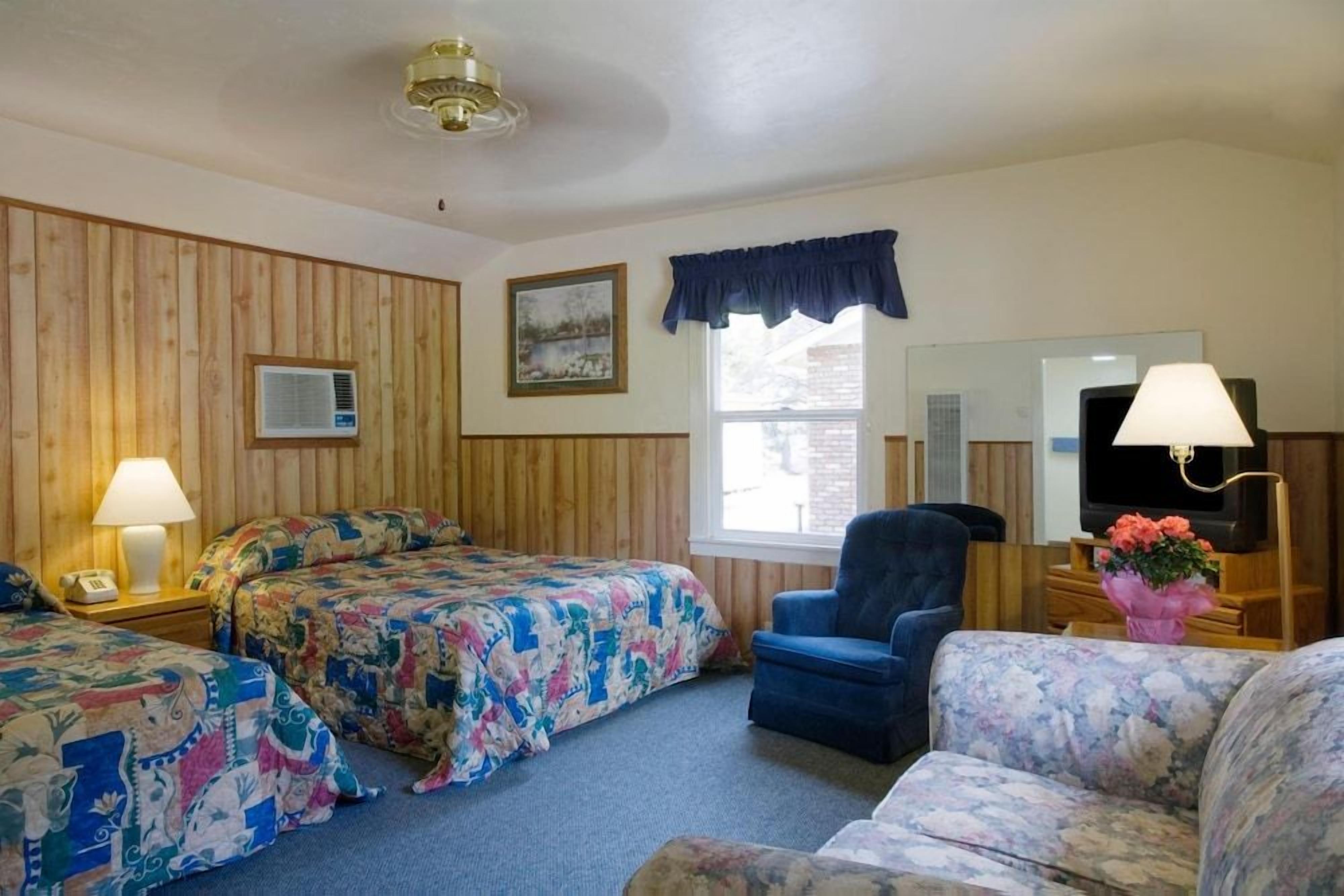 A hotel room with two beds, a sofa, a chair, a TV, a lamp, and a window with a view.