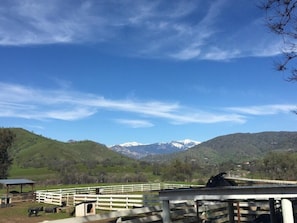 A fenced pasture with a stable and a small building, surrounded by green hills and snow-capped mountains under a clear sky. - Lazy J Ranch-americas Best Value Inn (Three Rivers)