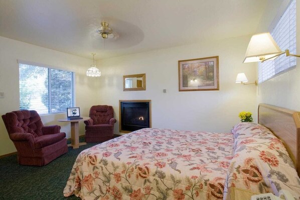 A hotel room with a bed, two armchairs, a fireplace, a chandelier, and a painting on the wall. - Lazy J Ranch-americas Best Value Inn (Three Rivers)