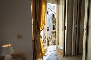 A room with a bed, a bedside table with a lamp, and a window with curtains. - La Cantunera by Biddizzi Rari - inside the historic district of “Cadda” (Sciacca)