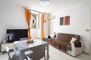 Ein Wohnzimmer mit Flachbildfernseher, einem Esstisch mit Stühlen, einer Couch und einer Klimaanlage an der Wand.