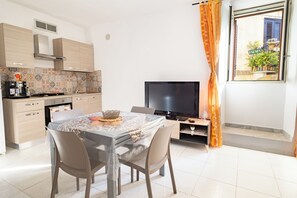 A modern kitchen with a dining area, a flat-screen TV, and a window with curtains. - La Cantunera by Biddizzi Rari - inside the historic district of “Cadda” (Sciacca)